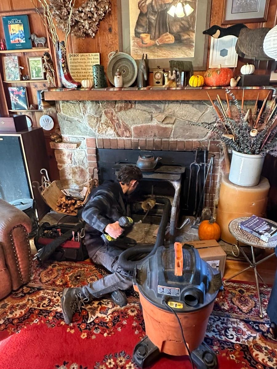 Best Chimney LLC technician sweeping a stone fireplace from inside a living room with a HEPA shop vacuum and floor protection in place